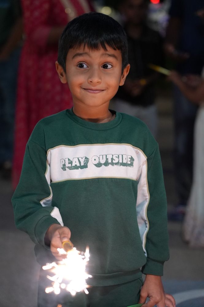 A smiling boy holding a lit sparkler at the temple’s Diwali celebration